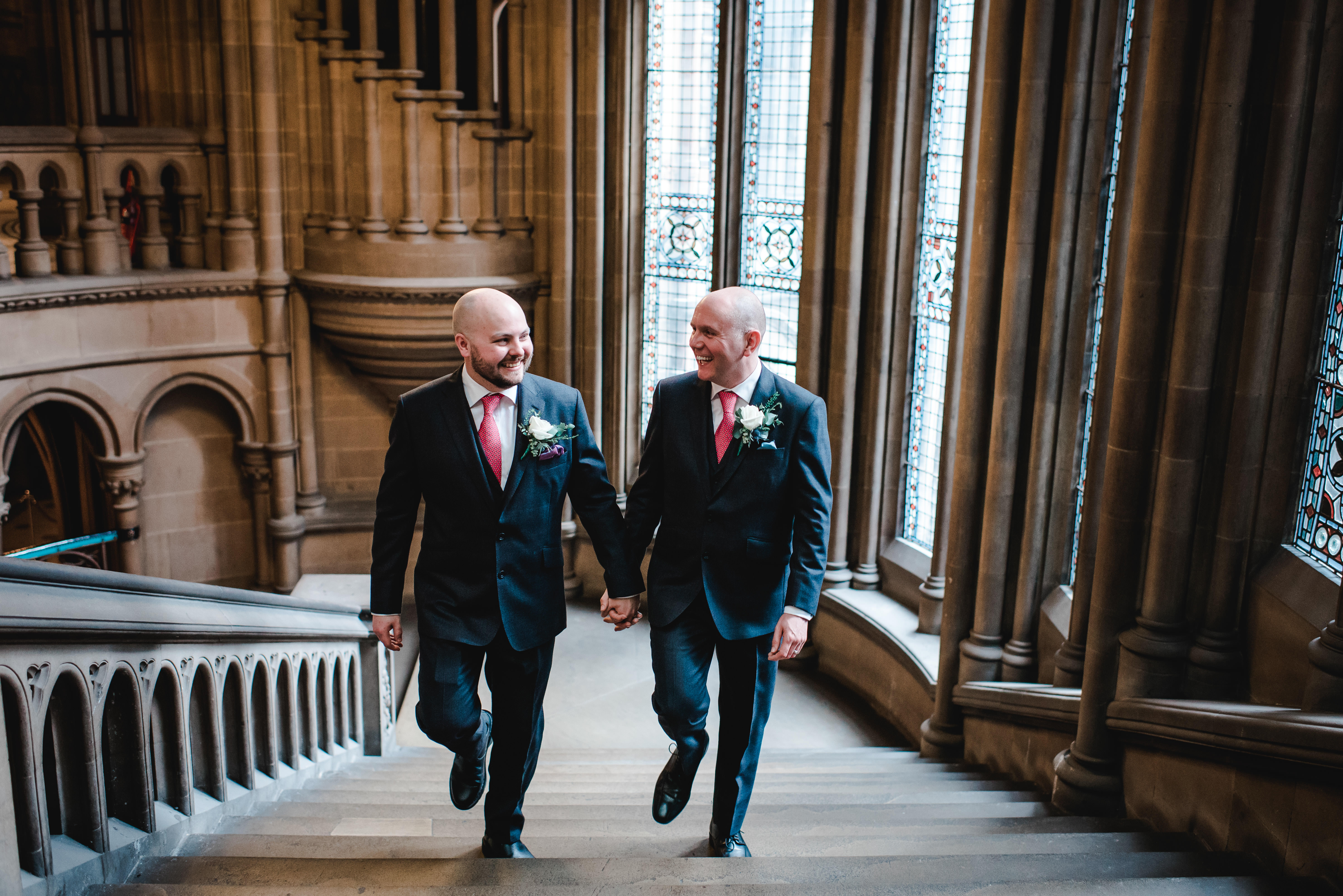 Groom and groom holding hands walking up main stairs in Manchester Town Hall wedding
