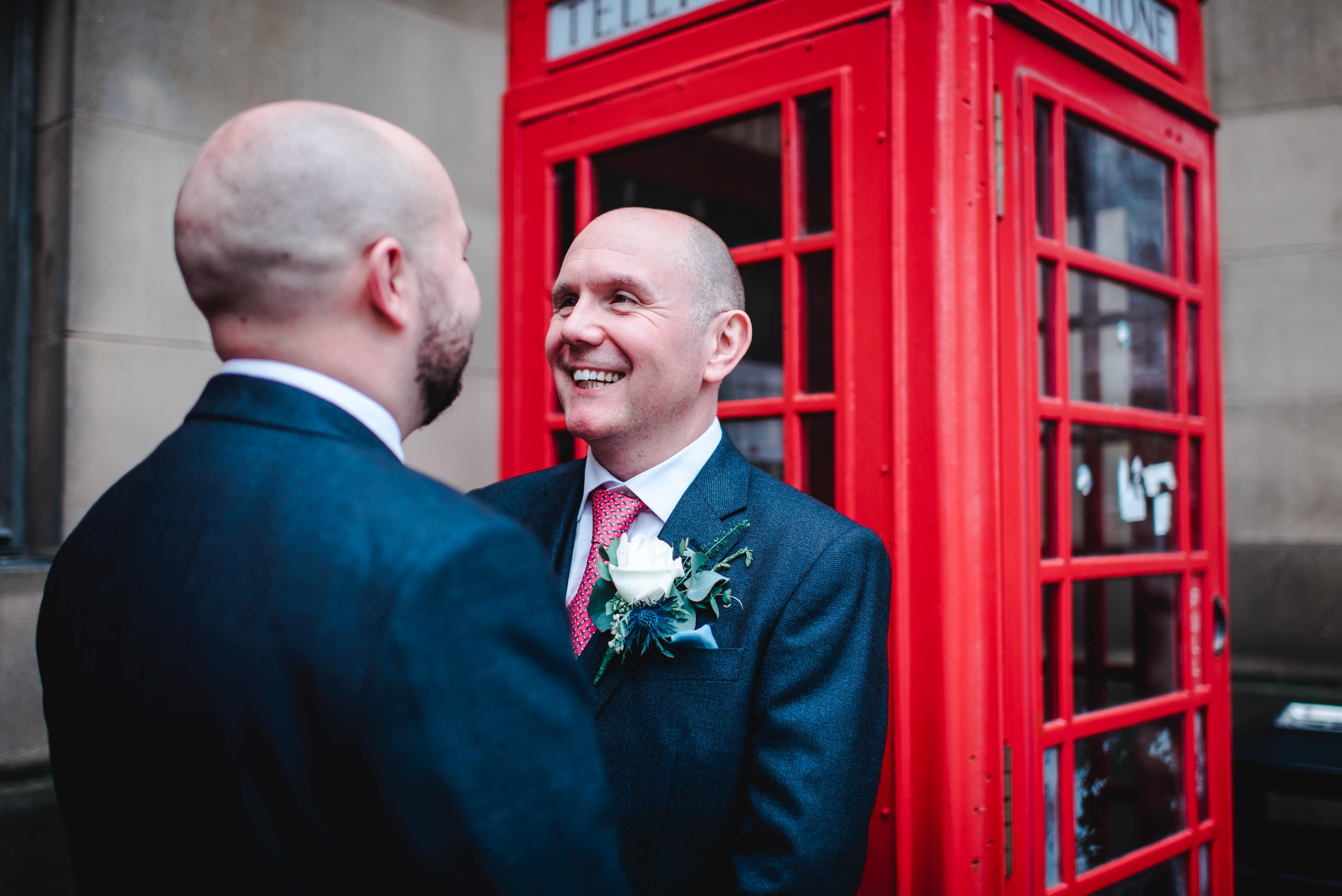 Groom smiling at wedding in front of red telephone box in Manchester